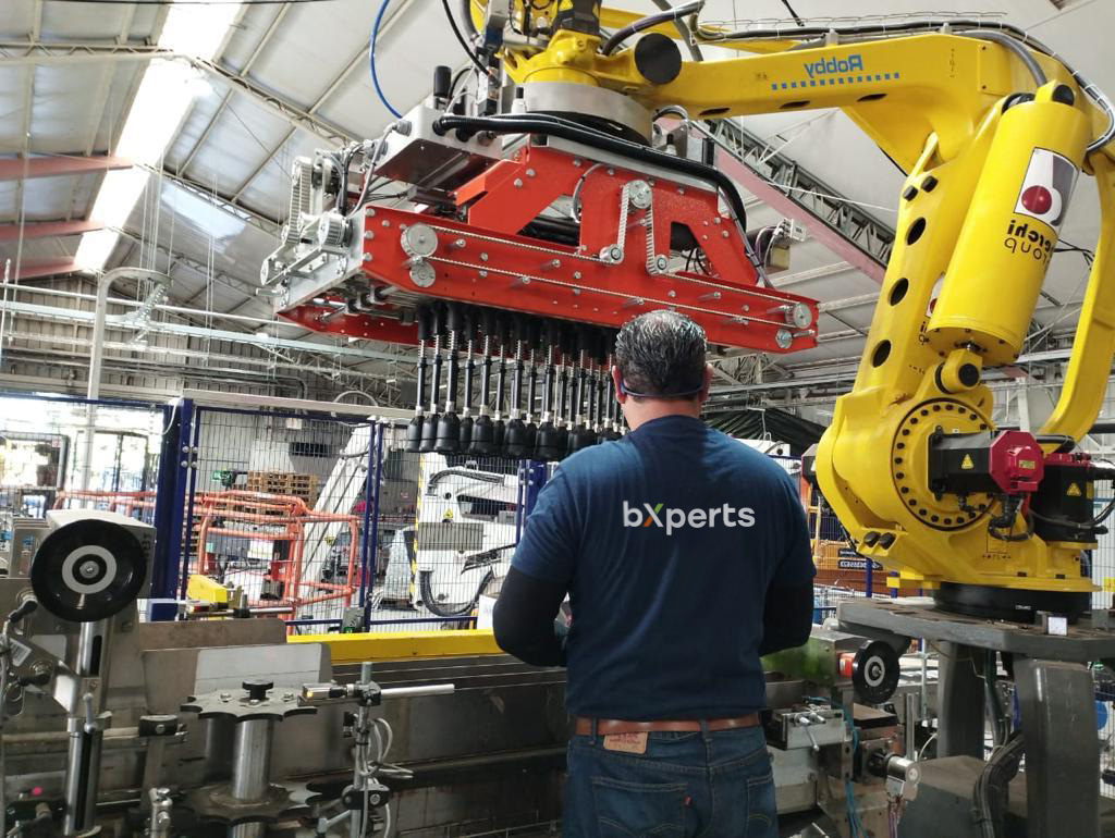 Tres técnicos de bXperts con chalecos de alta visibilidad naranja y cascos trabajando juntos en andamios industriales o instalación de estructura aérea
