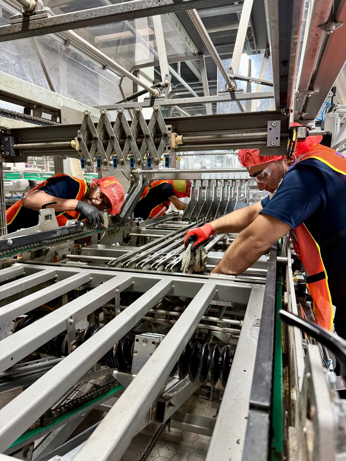 Three bXperts technicians in safety gear cleaning and inspecting industrial production equipment