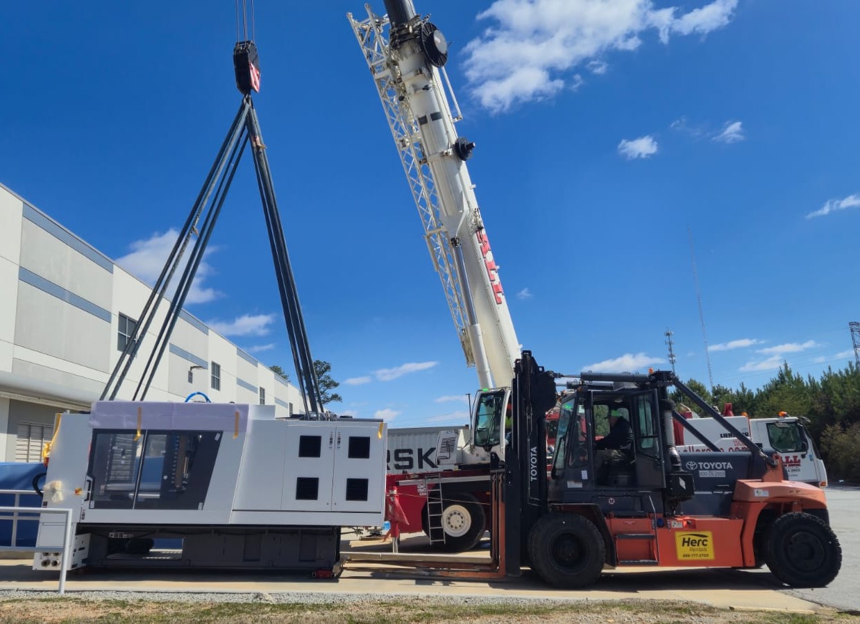 Crane and forklift working together to lift and position a large piece of industrial equipment
